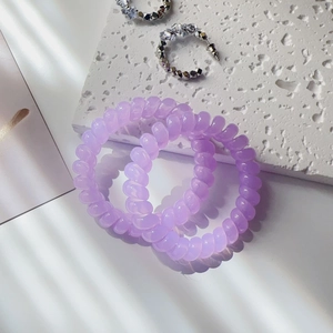Three purple spiral hair ties on a stone slab with leaf shadows and jewelry decor