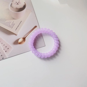 Close-up of a flexible purple spiral hair tie on a minimalist fashion magazine backdrop