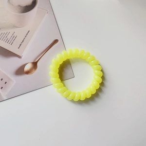 Detailed close-up of a bright yellow spiral elastic telephone wire hair tie on a white surface