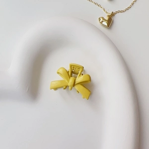Close-up of a matte yellow bow hair claw clip displayed on a white heart-shaped plate