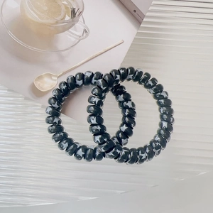 Close-up of black telephone cord hair ties with white star patterns on a glass tray