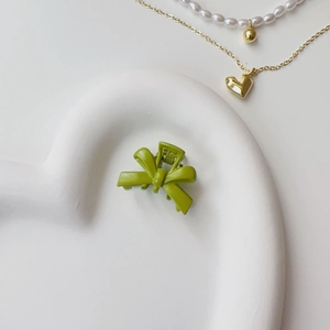 Close-up of a matte grass green bow hair claw clip on a white heart-shaped tray