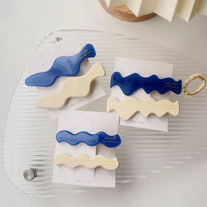 Nahaufnahme von wellenförmigen Acetat-Haarspangen in Blau und Beige auf Glastablett