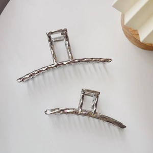 Close-up of two irregular silver liquid metal hair claws with lava texture and high shine