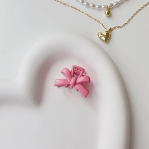 Pink bow-shaped hair clip with matte finish displayed on a white heart tray