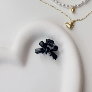 Detail shot of a glossy black bow hair clip on a heart-shaped tray with jewelry