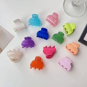 Flat lay of 12 colorful mini matte hair claws with metal springs on a white background