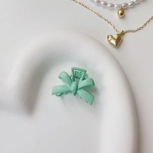 Detail of mint green bow hair clip on ceramic tray with golden jewelry accents