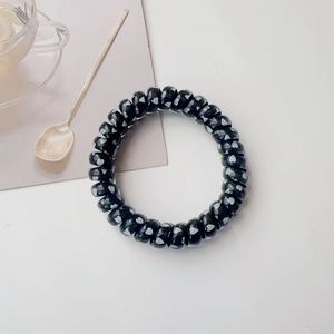 Detail of black spiral hair tie with white hearts on a clean minimalist background