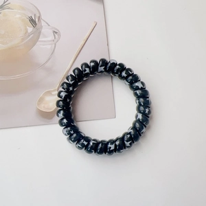 Detailed close-up of a black spiral hair tie featuring white star patterns on a desk