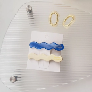 Detailansicht welliger Acetat-Haarspangen und goldener ovaler Ohrringe auf Karte