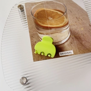 Close-up of neon green mini matte claw clip on a stylish transparent display stand