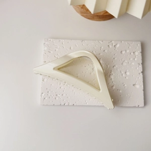 Détail de la pince à cheveux triangulaire crème sur socle en pierre texturée