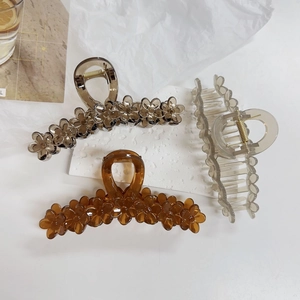 Three acrylic flower hair claws in amber and gray tones on a clean background