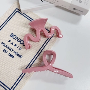 Détail de deux pinces à cheveux rose Morandi aux motifs vagues et croisés sur tissu