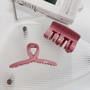 Détail de deux pinces à cheveux roses mates sur un support en acrylique avec un livre