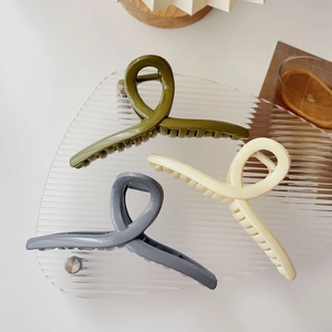 Detailed view of three large matte hair claw clips in olive green, cream, and grey blue