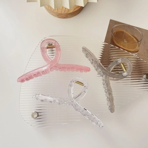 Three oversized translucent resin hair claws in pink, grey and clear on a tray