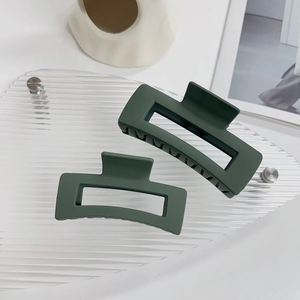 Dettaglio di due mollette per capelli rettangolari verde scuro opaco su vassoio