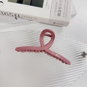 Détail d'une pince à cheveux rose mat au design minimaliste croisé sur un plateau en verre