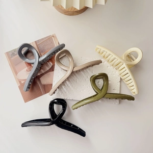 Flat lay of five glossy oversized hair claws in neutral colors on textured stone