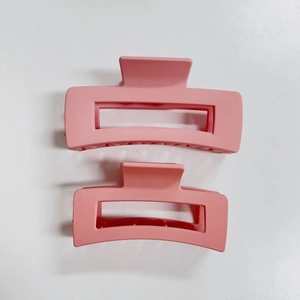 Dettaglio di due pinze per capelli rettangolari rosa opaco con design vuoto su fondo bianco