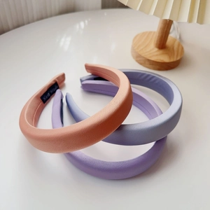 Close-up of three padded sponge headbands in pink, blue, and purple with satin texture
