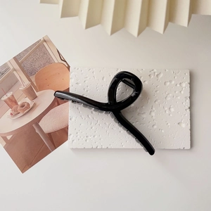 Close-up of a large black glossy hair claw clip on a stylish decorative stone background