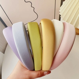 Hand holding a set of six colorful padded sponge headbands in soft pastel fabric textures