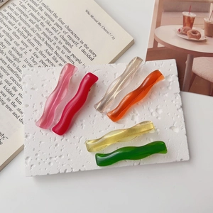 Close-up of six colorful wave-shaped resin hair clips on a textured white surface