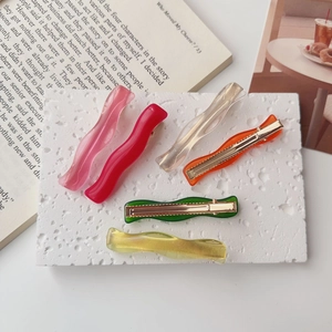Detailed view of six colorful wavy resin hair clips set on a textured white stone surface