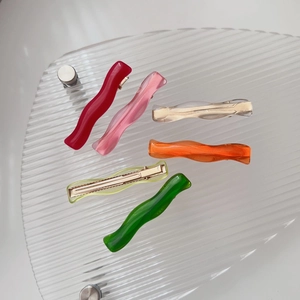 Close-up of colorful wavy resin hair clips set with gold metal duckbill clips on tray