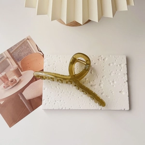 Close-up of olive green oversized hair claw clip on a minimalist white stone surface