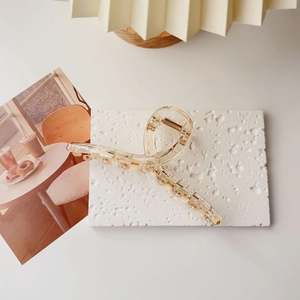 Detail of transparent amber-dotted hair claw clip on white textured stone background