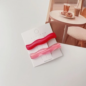 Detail of red and pink translucent resin wave hair clips on a white branding card