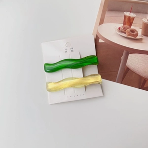 Detail of green and amber wavy resin hair clips on a white display card in macro view