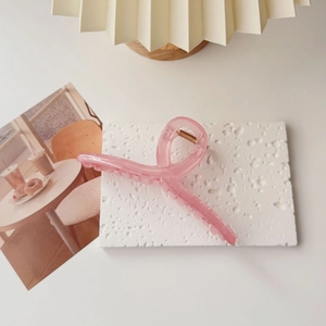 Detailed view of an oversized pink translucent shark hair claw clip on a white textured board