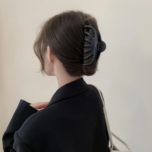 Macro detail of large matte black hair claw clip securing a thick bun on model