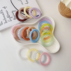 Assorted colorful spiral phone cord hair ties set on a white ceramic tray and book