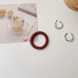 Brown spiral hair tie and silver hoop earrings on a minimalist white table setting