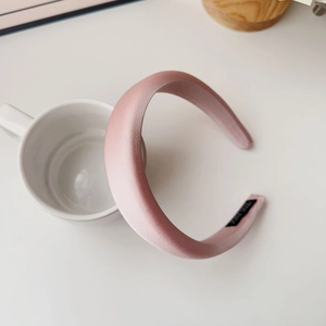 Detailed shot of pearly pink padded satin headband with handmade label on a white table