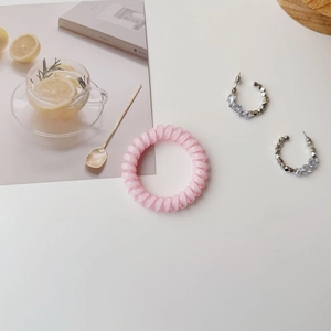 Flat lay of transparent pink spiral hair tie and silver C-shaped zircon earrings