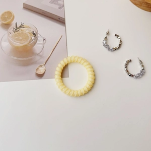 Pale yellow spiral hair tie and silver beaded C-shaped earrings on a Paris themed setup
