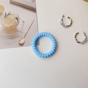 Blue spiral phone cord hair tie and silver crystal hoop earrings on a clean white desk
