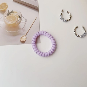 Close-up of translucent purple spiral hair tie and beaded earrings on a white surface