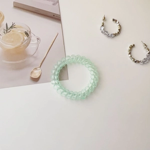 Close-up of a light green spiral hair tie and beaded crystal C-shaped earrings