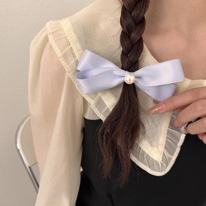 Dettaglio di un fermaglio per capelli a fiocco in raso lilla con perla su una treccia