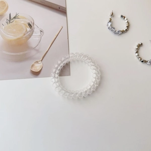 Transparent spiral hair tie and silver geometric crystal earrings on white desk