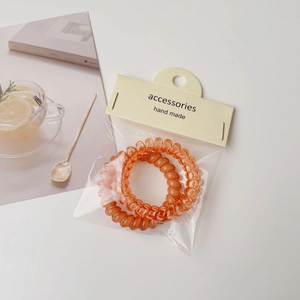 Detail of two orange spiral hair ties with packaging on a minimalist white background