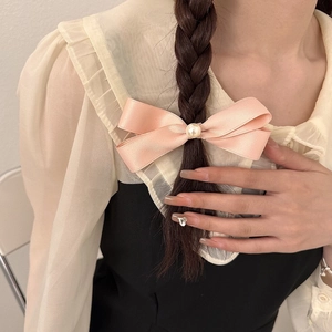 Dettaglio di fermagli a fiocco in raso rosa con perle su capelli intrecciati